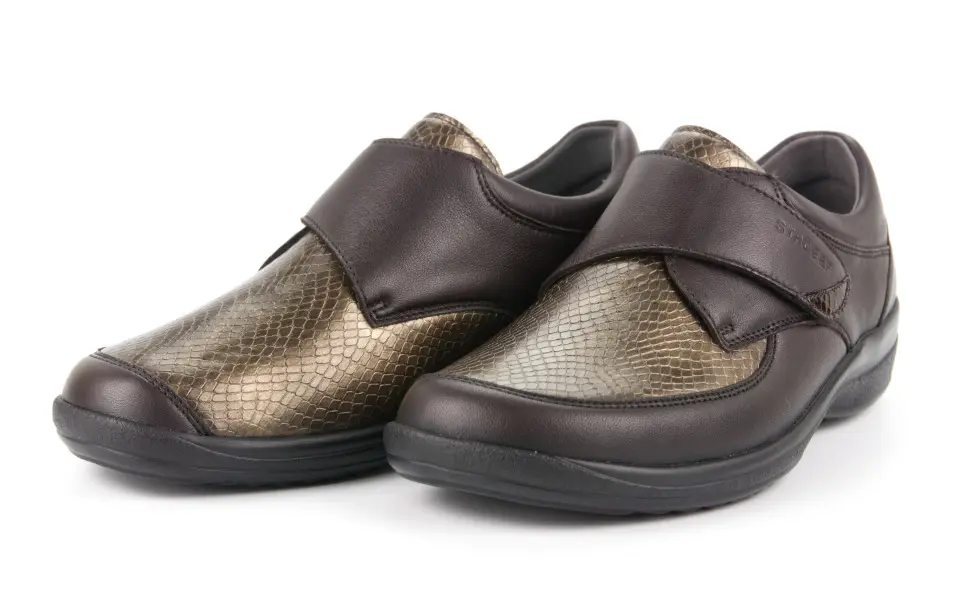 Der Schuh MURIEL LammNappa Stretch in Espresso liegt elegant auf einer hellen Oberfläche, umgeben von sanftem Licht, das seine Textur betont.