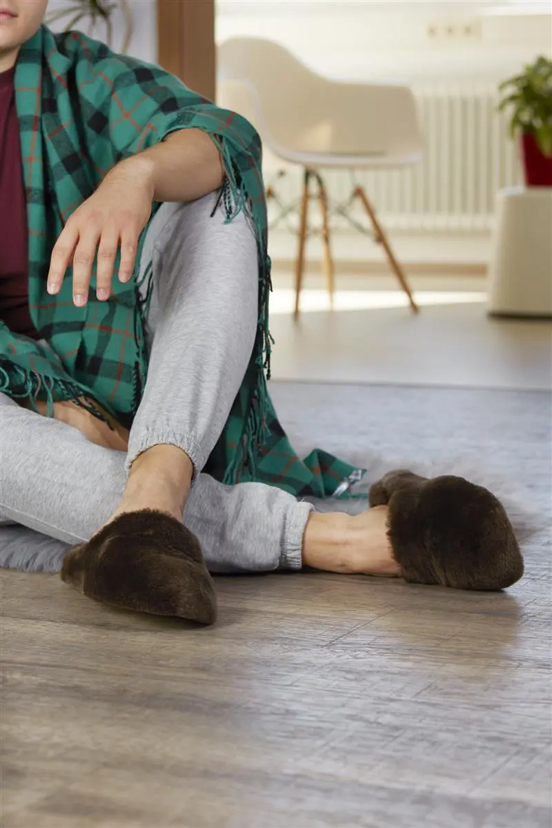 Der Schuh THOMAS aus Lammfell in dunkelbraun zeigt sich bequem und stilvoll, perfekt für entspannte Stunden zu Hause.