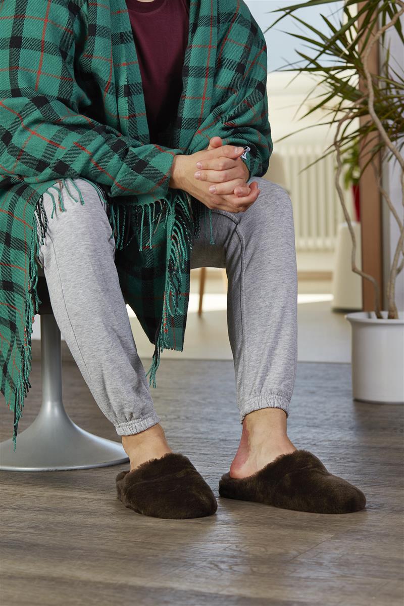 Der THOMAS Schuh aus weichem Lammfell in dunkelbraun ruht auf einem hellen Untergrund, ideal für gemütliche Stunden zu Hause.