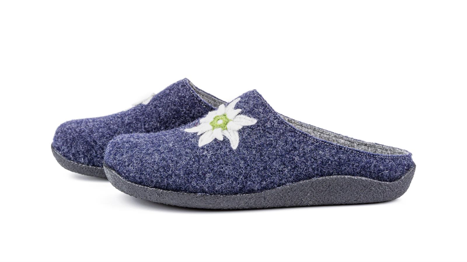 Der Schuh VRONI aus grauem Filz mit einem Edelweißmotiv, seitlich und leicht schräg präsentiert. Ideal für gemütliche Anlässe.